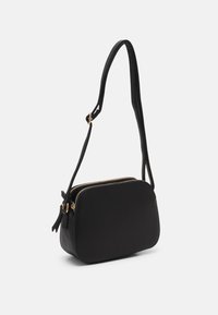 Černá crossbody taška s texturovaným povrchem, zaobleným tvarem, dvojitým zipem a tenkým nastavitelným popruhem se zlatými kovovými prvky.