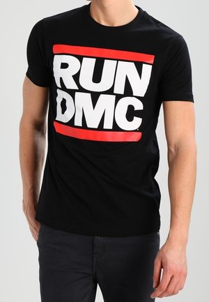 Mann trägt ein schwarzes T-Shirt mit einem markanten weißen "RUN DMC"-Logo, eingerahmt von zwei horizontalen roten Linien.