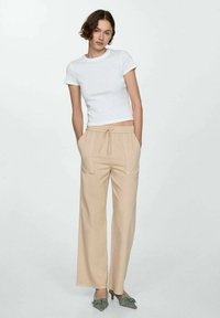 Witte kortebloezende getailleerde t-shirt gecombineerd met beige wijde broek met elastische tailleband en twee voorkeeltas.