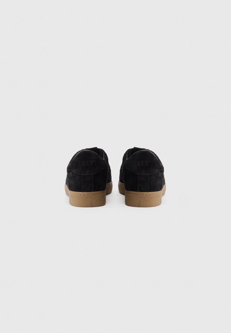 Baskets en suède noir avec une finition texturée, semelles en caoutchouc et une marque discrète sur le talon ; conçues pour un usage décontracté et le confort.