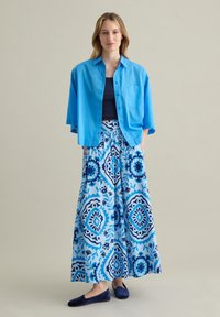 Camisa azul de botones, top de tirantes azul marino, falda larga con patrones florales azules y zapatos planos azules. Tela liviana y diseño casual.