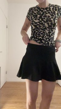 Saia preta em formato evasê, feita de um tecido leve, combinada com um top justo de padrão de leopardo. O design apresenta um detalhe franzido na cintura.
