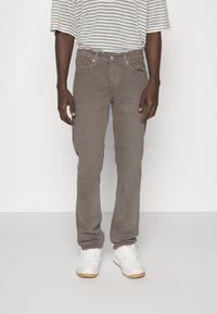 Šedé džíny z denimu s rovnými nohavicemi, pěti kapsami a kovovými detaily. Model má na sobě šedé pruhované tričko a bílé tenisky.