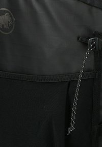 Acercamiento de un bolsillo de mochila negra para exterior con cordón ajustable y un tenue logo de mamut en la tela texturizada.