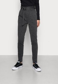 Pantalons gris ajustés en tissu texturé, avec un lien �à la taille et des poches avant, associés à des baskets noires avec des semelles blanches.