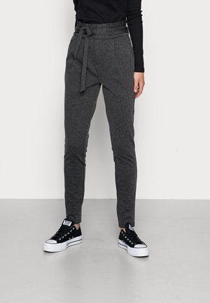 Pantalons gris ajustés en tissu texturé, avec un lien à la taille et des poches avant, associés à des baskets noires avec des semelles blanches.