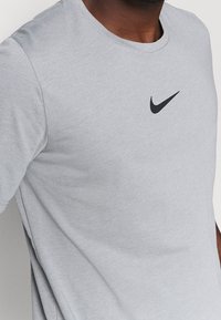 Camiseta de algodón gris claro con escote redondo y mangas cortas. Presenta un pequeño logo de la marca Nike en negro en el pecho.