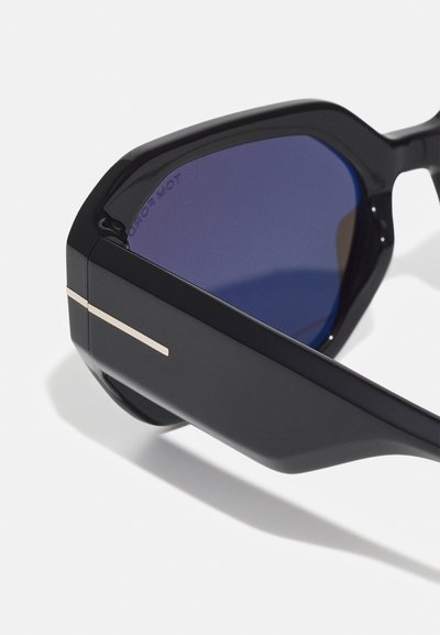 Ochelari de soare cu un cadru din plastic negru, lentile colorate în violet și un accent subțire din metal auriu pe lateral. Design unghiular cu o finisare texturată.