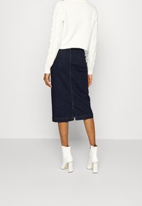 Mörk denim midi kjol med en slits bak och rak passform, kombinerad med en vit kabelstickad tröja och vita ankelboots.