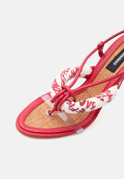 Sandale rouge à talons hauts avec semelle intérieure tissée, boucle d'orteil coussinée en tissu avec texte rouge, fines lanières de cheville et lanières de soutien en plastique transparent.