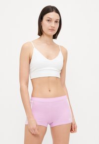 Balta sporta krūšturis ar plānām siksnām, apvienots ar gaiši rozā šortiem ar baltām sānu svītrām un mazu logo apakšmalā.