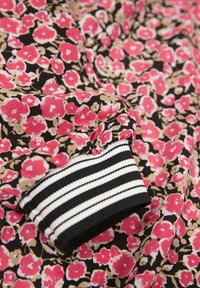 Tkanina z różowym i beżowym wzorem kwiatowym na czarnym tle, z czarnym i białym paskowanym elastycznym mankietem.