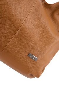 Braune Kunstleder-Handtasche mit strukturiertem Oberflächen, Reißverschluss und einem Metall-Logo-Schild. Runde Form mit einem lässigen Design.