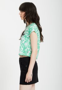 Groen en wit patroon shirt met korte mouwen, waarvan de onderkant is afgeknipt, gecombineerd met een zwarte denim rok met een rafelige zoom. Eenvoudige zilveren ketting zichtbaar.