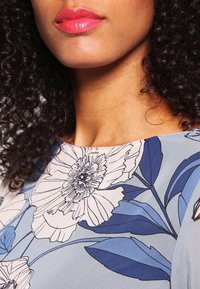 Light blue floral blouse featuring large white and dark blue flower patterns, smooth texture, and a round neckline.