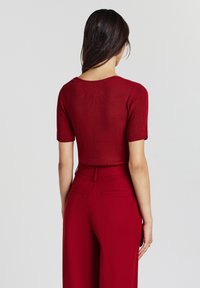 Top rosso a righe con maniche corte abbinato a pantaloni larghi rossi a vita alta. Il top presenta un collo arrotondato e una silhouette aderente.