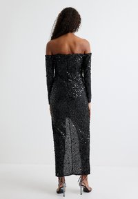 Zwarte, off-shoulder avonddress versierd met pailletten, met lange mouwen en een hoge split aan de achterkant.