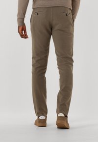 Slim-fit, beige cotton trousers with two back pockets, visible stitching, and a smooth texture, paired with brown suede shoes.