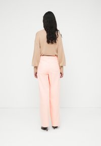 Φαρδιά τζιν παντελόνια σε ανοιχτό ροζ χρώμα με πίσω τσέπες, συνδυασμένα με μπεζ πλεκτό πουλόβερ με μπαλόν μανίκια. Οπίσθια όψη που αναδεικνύει το σχέδιο του ενδύματος.