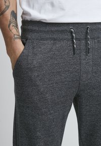 Dark gray sweatpants made of textured fabric, featuring an elastic waistband with drawstrings and side pockets.