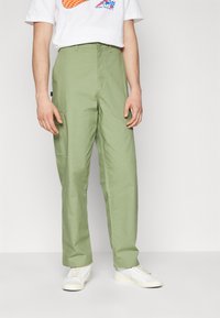 Grønne cargo-bukser med afslappet pasform, tekstur mønster og sidelommer, parret med hvide sneakers og en grafisk t-shirt.