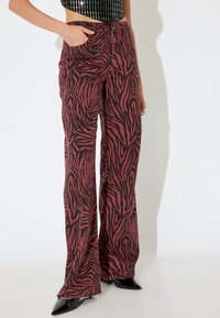 Pantalons larges de couleur rouille avec un motif zèbre noir. Fabriqués en tissu léger, dotés de deux poches latérales et d'une taille cintrée.