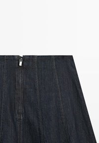 Gonna in denim blu scuro con cerniera frontale argentata e dettagli di cuciture verticali, mostrata su sfondo bianco.