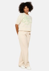 Light beige sweater with short sleeves and green floral design, paired with beige pants and white sneakers. Soft texture, relaxed fit.