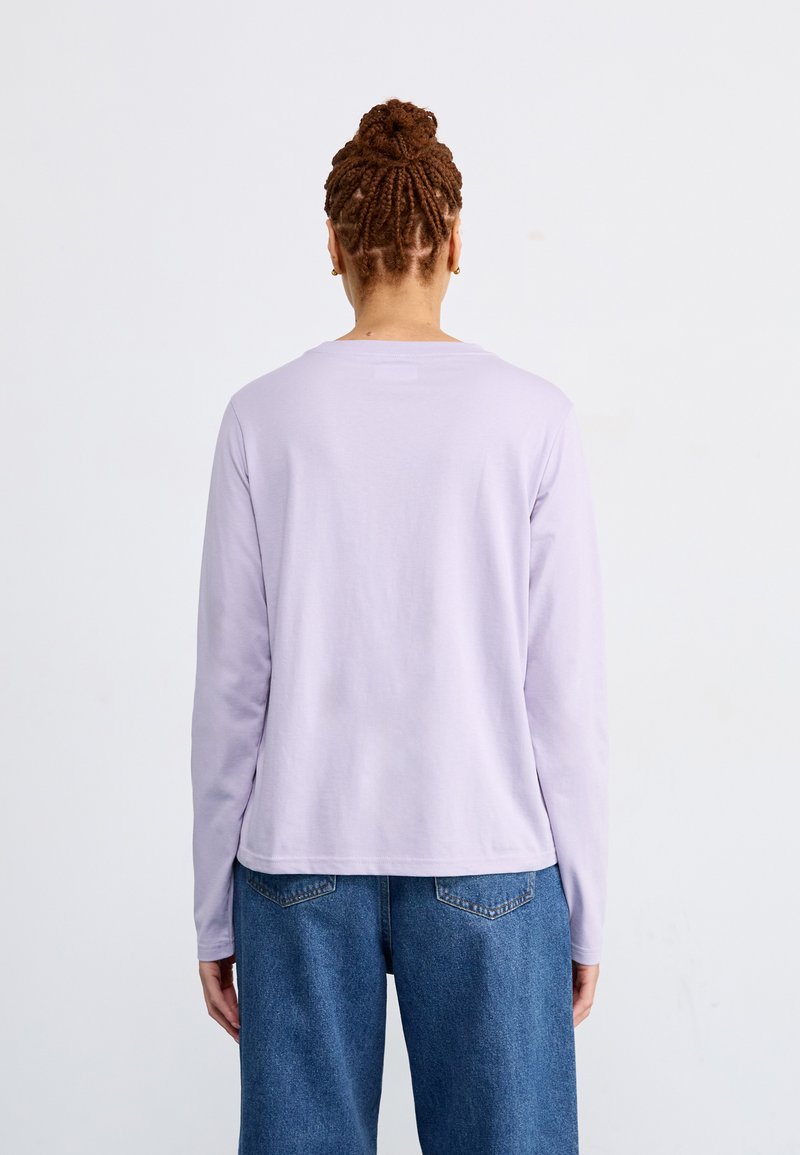 Camisa de manga larga en color lavanda con cuello redondo, hecha de una tela suave. Combinada con unos vaqueros azul de cintura alta que tienen bolsillos traseros.