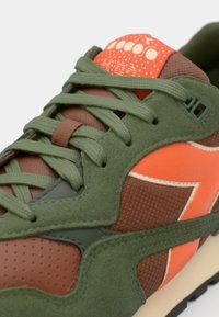 Retro athletic sneaker featuring a mix of green suede, brown mesh, and orange accents. Textured surfaces with a patterned tongue and laces.