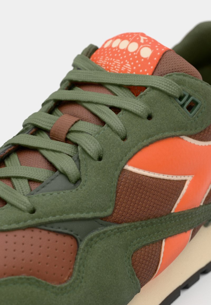 Retro-Sportler-Sneaker mit einer Kombination aus grünem Wildleder, braunem Mesh und orangefarbenen Akzenten. Strukturierte Oberflächen mit einer gemusterten Zunge und Schnürsenkeln.