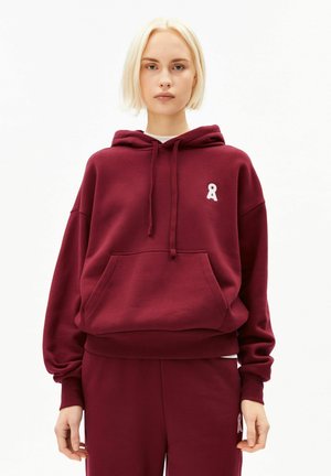 Sweat à capuche bordeaux avec une poche avant, des poignets côtelés et un logo en ruban blanc sur la poitrine gauche. Tissu doux et texturé.