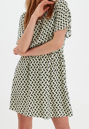 Woman wearing short-sleeve knee-length dress with black and white geometric chevron pattern, arms crossed and hand near face.