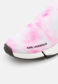 Růžová a bílá síťovaná teniska s texturovaným svrškem, výrazným logem a rozdělenou černou gumovou podrážkou. Disponuje moderním, elegantním designem.