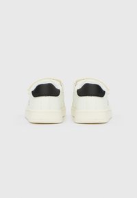 Par belih superg s črnimi petnimi zavesami, videnih od zadaj, postavljenih na enostavno svetlo sivo ozadje.