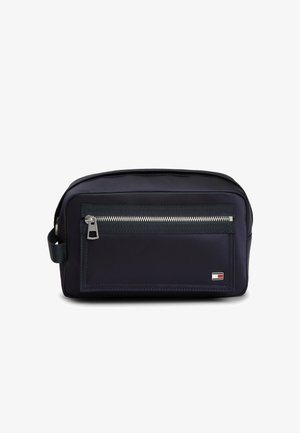 Kompakt sort toilettaske med frontlynlåslomme, sidehåndtag og lille rektangulært logo i rød, hvid og blå i nederste højre hjørne.