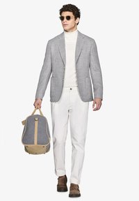 Rutet blazer med grå og hvid mønster, hvid turtleneck, hvide bukser, brune sko, bærer en grå og tan rygsæk.