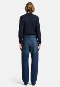 Granatowa koszula z długim rękawem i luźne niebieskie dżinsy. Dżinsy mają prosty krój nogawki i dwie tylne kieszenie. Jednolite kolory, minimalne detale.