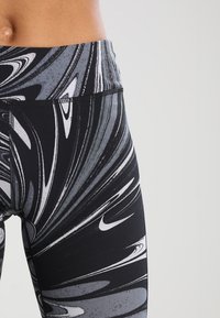 Černé a šedé legíny s vířivým designem, vyrobené z elastického materiálu, s vysokým pasem a jemným bílým logem.