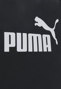 Zwarte stof met een groot wit "PUMA" logo en een springende katachtige embleem, beide prominent aanwezig. Gladde textuur, modern ontwerp.