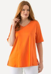 Maglietta arancione a maniche corte con scollatura a V e rifiniture decorative lungo il collo, caratterizzata da una vestibilità comoda e fessure laterali per facilità di movimento.