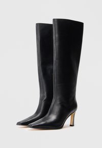 Bottes en cuir noir jusqu'au genou avec un bout pointu, un talon aiguille fin et une texture lisse, dotées d'une fermeture éclair sur le côté.