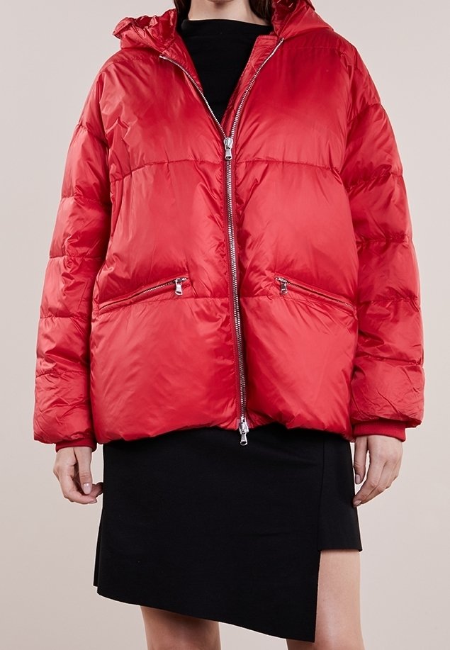 Rød polstret jakke med hætte, med lynlås foran, to lynlåslommer og en puffet tekstur. Båret over en sort nederdel.