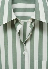 Chemise à col avec des rayures verticales vertes et blanches, avec des boutons blancs et une poche poitrine visible.