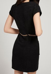 Abito nero con tessuto testurizzato, maniche corte e una forma fitted. Presenta una cintura in catena dorata che accentua la vita.