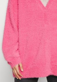 Fuzzy pink sweater with a V-neck, long sleeves, and a relaxed fit. The texture is soft and plush, with ribbed cuffs and hem.