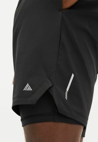 Svarta träningsshorts med fuktavledande tyg, sidofickor och vita logodetaljer på fållen för ökad rörelsefrihet och stil.