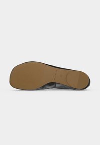 Semelle d'une chaussure plate noire avec une semelle en caoutchouc lisse beige et un petit patch circulaire au talon, taille 36 indiquée sur la semelle.
