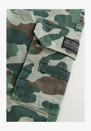 Zaļš un bēšs kamuflāžas audums ar izšūtu kabatu un birku. Tekstūrēta virsma, izturīga izšūšana un Velcro aizdare.