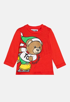 Camiseta roja de manga larga para niño pequeño con un dibujo animado de un oso patinando sobre hielo, que lleva un gorro verde y patines amarillos, con el texto "Moschino".
